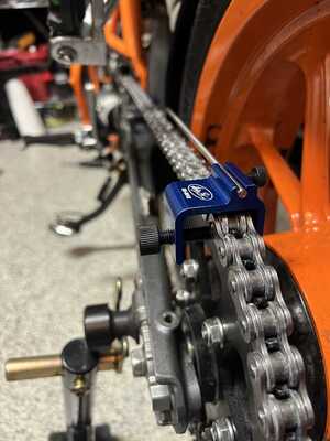 Shows a chain alignment tool mounted to the rear sprocket, with a straight rod pointing towards the front sprocket.